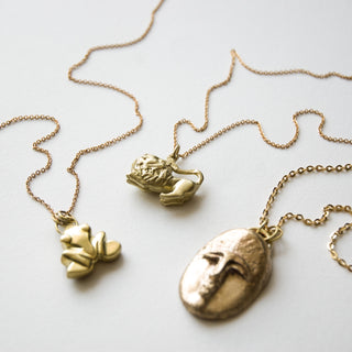 Recycled bronze and brass pendants with frog, lion, and face motifs on a flat white surface.