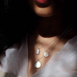 Model wearing a collection of pendants sustainably handmade by Lunaflux.