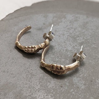 Recycled brass midi hoop earrings with an organic surface by Lunaflux on a grey stone background.